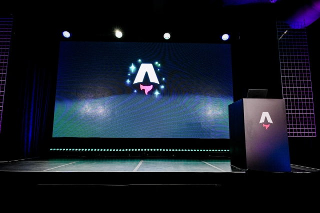 An empty stage with a large LED screen displaying the Astro Together logo. To the right, a black podium branded with the Astro logo.