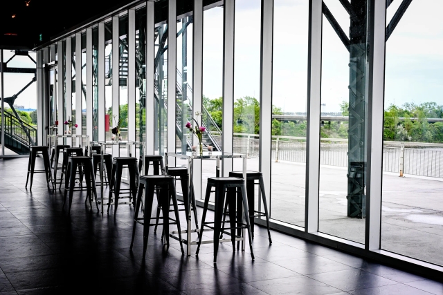 Several high tables and high chairs in front of floor-to-ceiling windows.