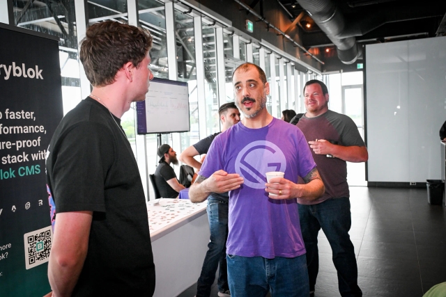 A representative wearing a purple Gatsby shirt speaking to a guest by the sponsor booths.