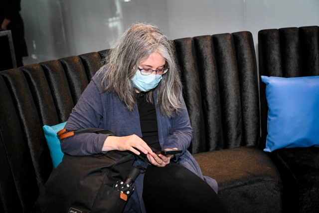 A woman wearing a mask, looking at her phone, while sitting in the Houston lounge.