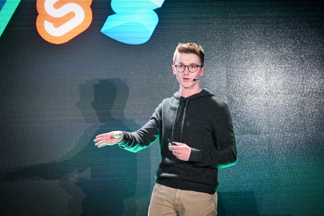 A close up of Ben Holmes on stage in front of a slide depicting logos of other frameworks.