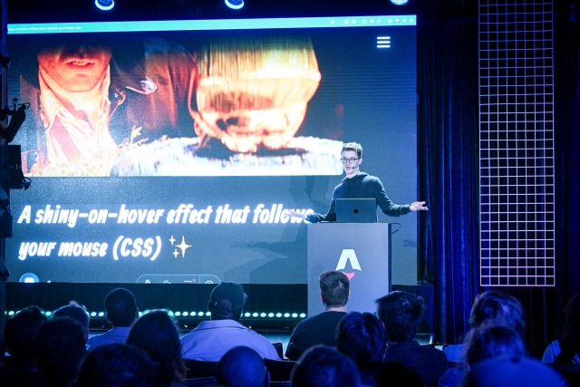 Ben Holmes stands behind an Astro branded podium on stage. He is sharing a demo.