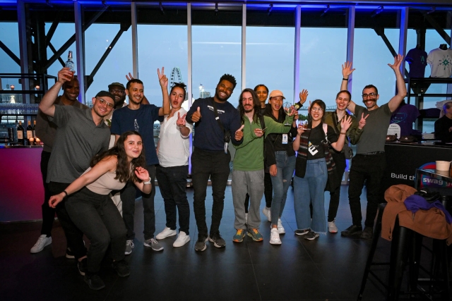 A large group of guests pose for a group photo in front of floor-to-ceiling windows.